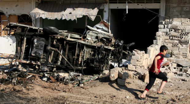 A boy runs past a damaged vehicle at a site hit by an airstrike in the rebel-held Tafas town, in Deraa Governorate, Syria.