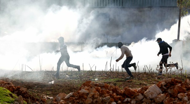 Palestinian protesters run for cover from teargas fired by Israeli troops during clashes in the West Bank village of Qusrah.