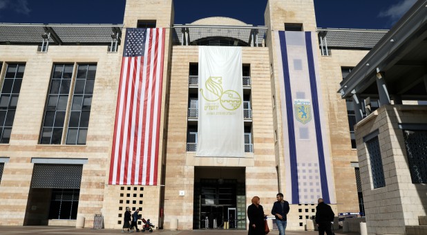 People walk at the Jerusalem's city hall as the American and Israeli national flags hang on the municipality building in Jerusalem.