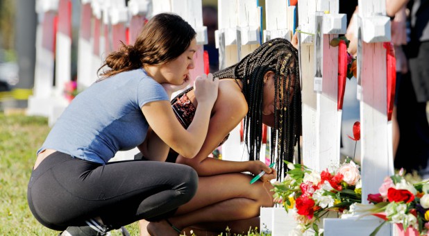 A senior at Marjory Stoneman Douglas High School weeps in front of a cross and Star of David for shooting victim Meadow Pollack while a fellow classmate consoles her at a memorial by the school in Parkland, Florida.