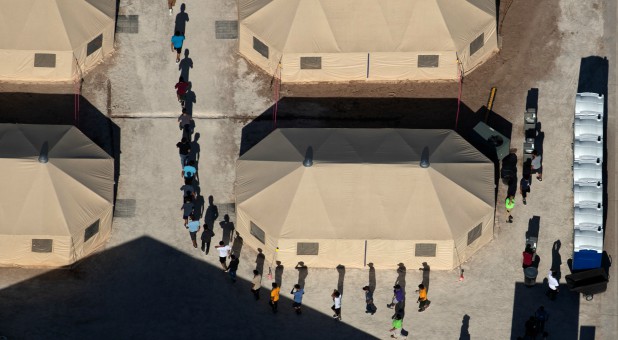 Immigrant children are led by staff in single file between tents at a detention facility next to the Mexican border.