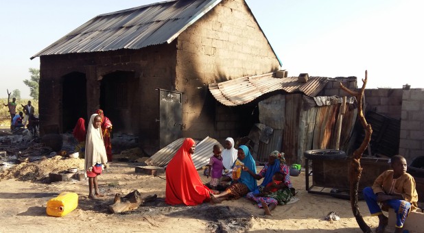 People sit near a burnt house after an attack by suspected members of the Islamist Boko Haram insurgency in Bulabulin village, Nigeria.